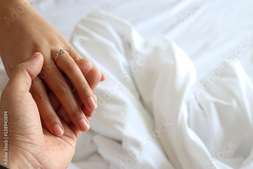 Partial view of couple in love holding hands while lying in bed white.
