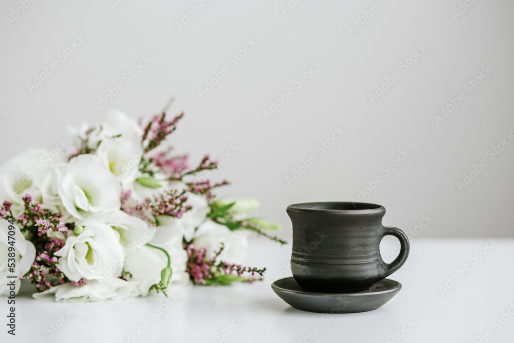 Black ceramic cup with coffee on table and bouquet of flowers. Black ceramic cup with coffee on table and bouquet of flowers.
