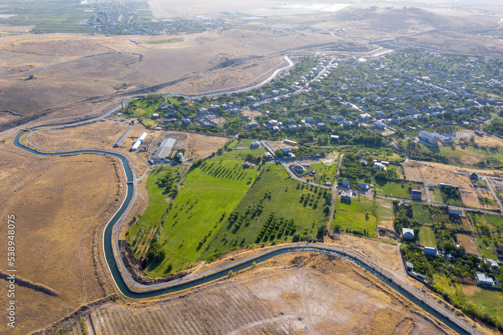 Aerial view of Arzni - Shamiram irrigation canal  banding Mrgashen village on sunny summer day. Kotayk Province, Armenia.