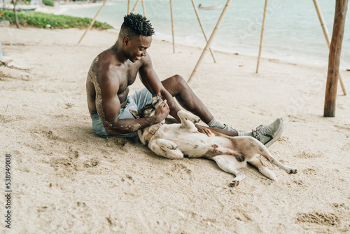 Smiling attractive young black man playing with a dog on the beach photo