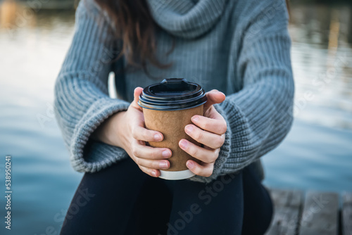 Close-up, a cup of coffee in the hands of a woman in nature near the river.