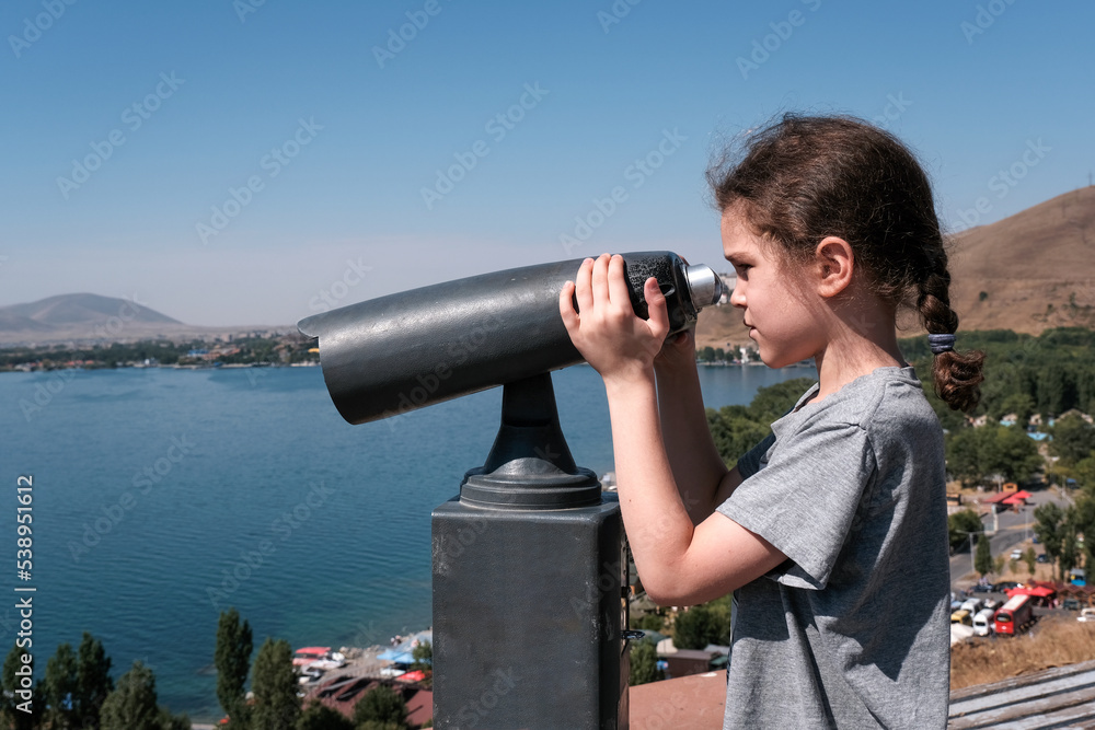10-year-old boy looks through coin operated binocular (binoscope) from Sevanavank monastery on sunny summer day. Sevan lake, Armenia.