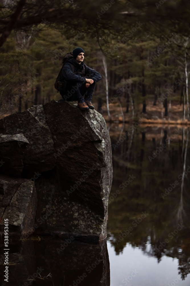 A caucasian man hiker sitting on a rock over looking a  lake in the forest watching reflections in the water.