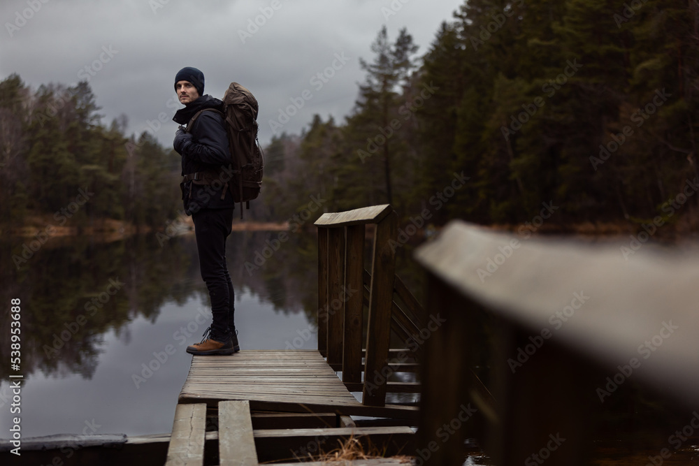 A caucasian man hiker standing on a wooden jetty over looking a  lake in the forest watching reflections in the water.