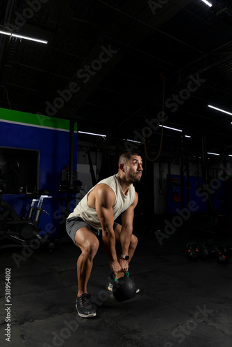 Vertical shot of a Latino man exercising in a gym using a kettlebell