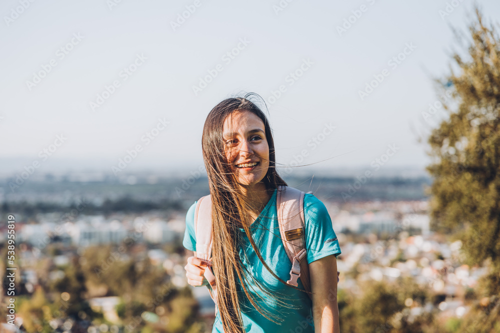 Smiling young woman with a backpack on the top of a the hill. Self-confidence. 