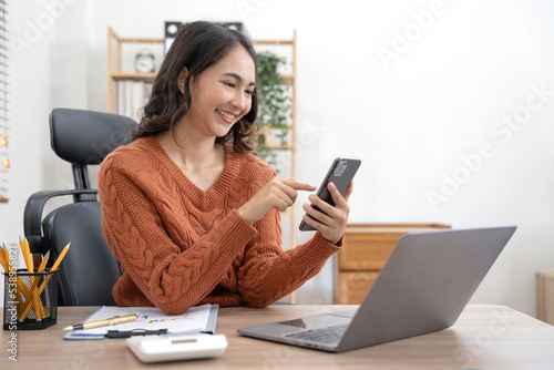 Smiling businesswoman using phone in office. Small business entrepreneur looking at her mobile phone and smiling, Young businesswoman holding a smartphone in a co-working space.