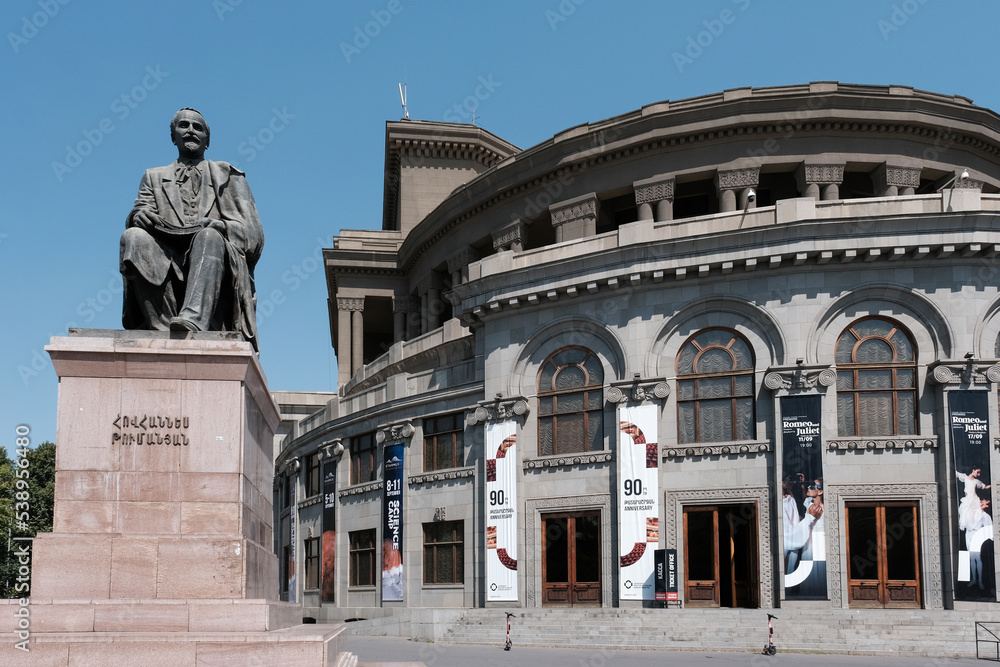 Armenian poet Hovhannes Tumanyan monument against Opera and Ballet Theatre on sunny day. Yerevan, Armenia.