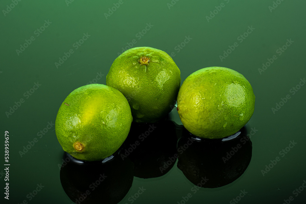three whole limes on dark glass with reflection