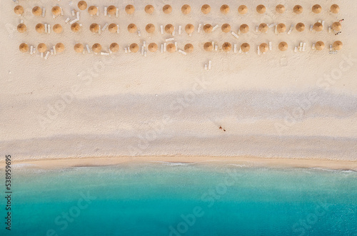 Sun umbrellas rows and sunbeds Myrtos Beach unique turquoise water seashore with a bright white pebbles often proclaimed as one of best beaches in Greece. Kefalonia island aerial background photo.