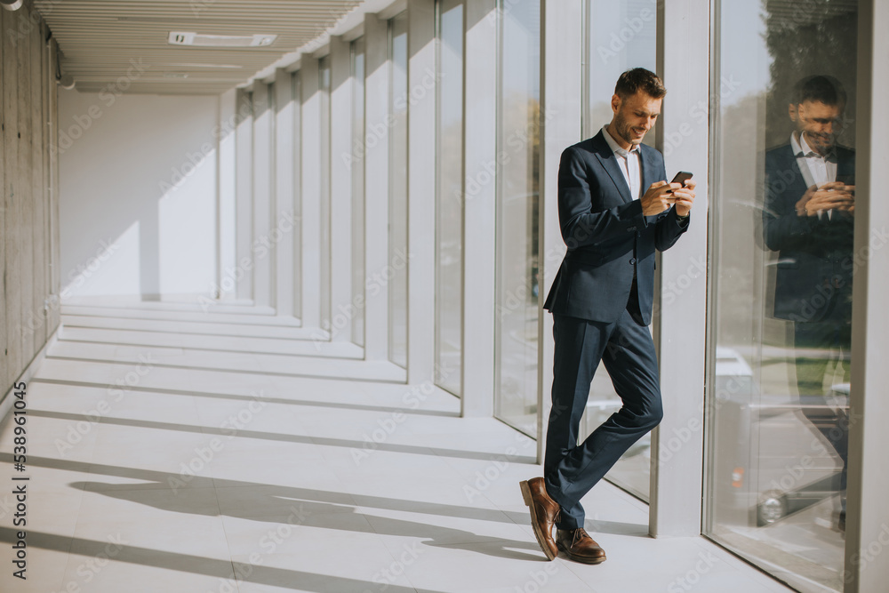 Young business man using mobile phone in the modern office hallway Young business man using mobile phone in the modern office hallway