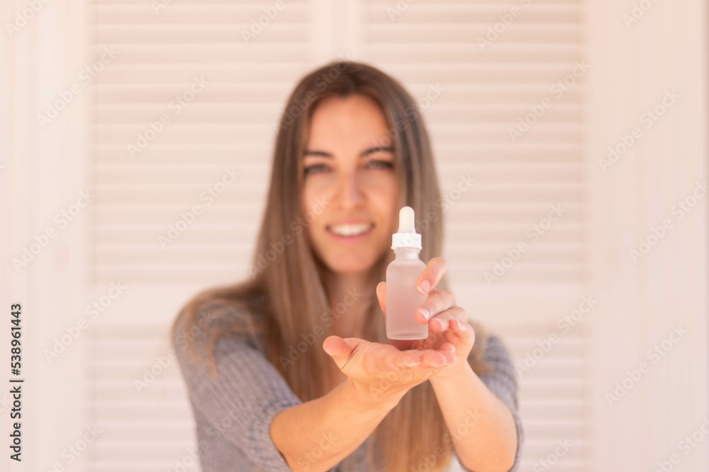 Front view of selective focus of unfocused young woman showing and holding hair oil container to the camera Front view of selective focus of unfocused young woman showing and holding hair oil container to the camera