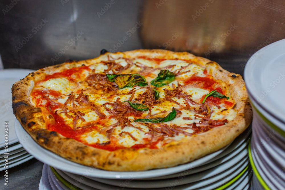 Pizza tradizionale napoletana con sugo di pomodoro, salame piccante, basilico, mozzarella e basilico pronta per essere servita in una pizzeria napoletana