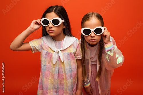 girls with serious face expressions adjusting sunglasses isolated on orange