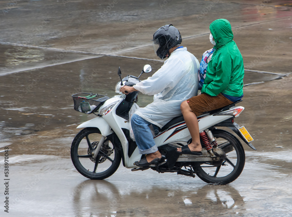 A couple in a raincoat is riding a motorbike on a wet road A couple in a raincoat is riding a motorbike on a wet road