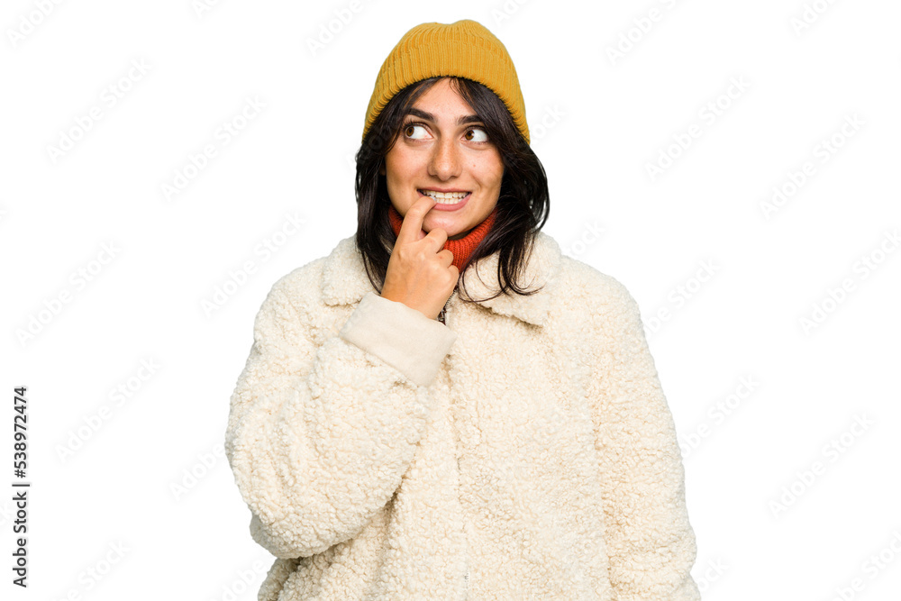 Young Indian woman wearing winter jacket and a wool cap isolated relaxed thinking about something looking at a copy space.