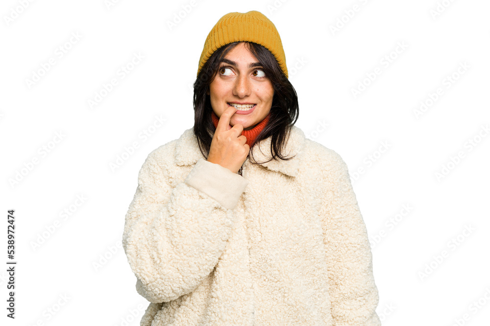 Young Indian woman wearing winter jacket and a wool cap isolated relaxed thinking about something looking at a copy space. Young Indian woman wearing winter jacket and a wool cap isolated relaxed thinking about something looking at a copy space.