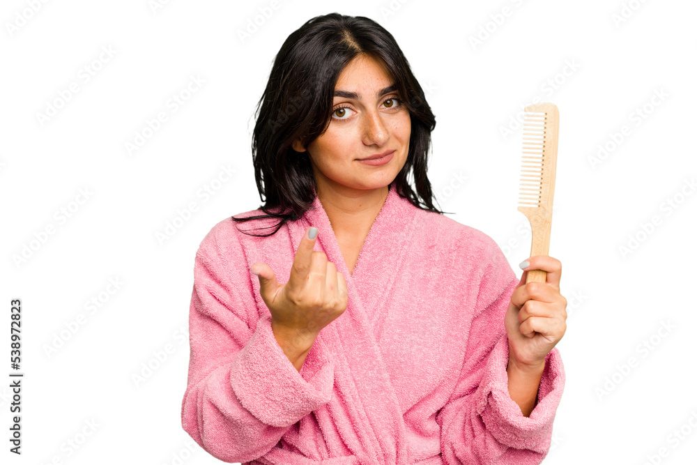 Young woman in a bathrobe holding an hair comb isolated pointing with finger at you as if inviting come closer. Young woman in a bathrobe holding an hair comb isolated pointing with finger at you as if inviting come closer.