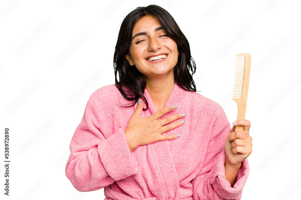 Young woman in a bathrobe holding an hair comb isolated laughs out loudly keeping hand on chest. Young woman in a bathrobe holding an hair comb isolated laughs out loudly keeping hand on chest.