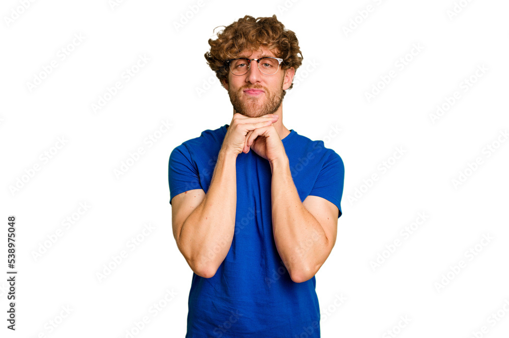 Young caucasian man isolated on green chroma background keeps hands under chin, is looking happily aside.