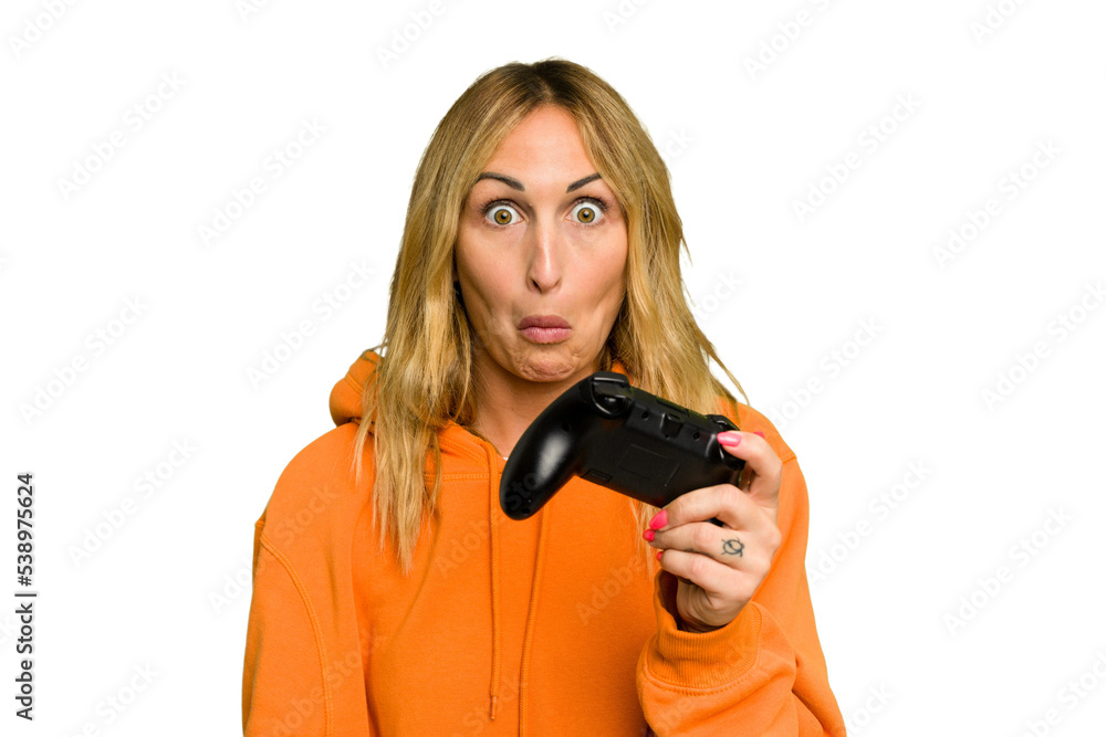 Young caucasian gamer woman holding a game controller isolated on green chroma background shrugs shoulders and open eyes confused. Young caucasian gamer woman holding a game controller isolated on green chroma background shrugs shoulders and open eyes confused.