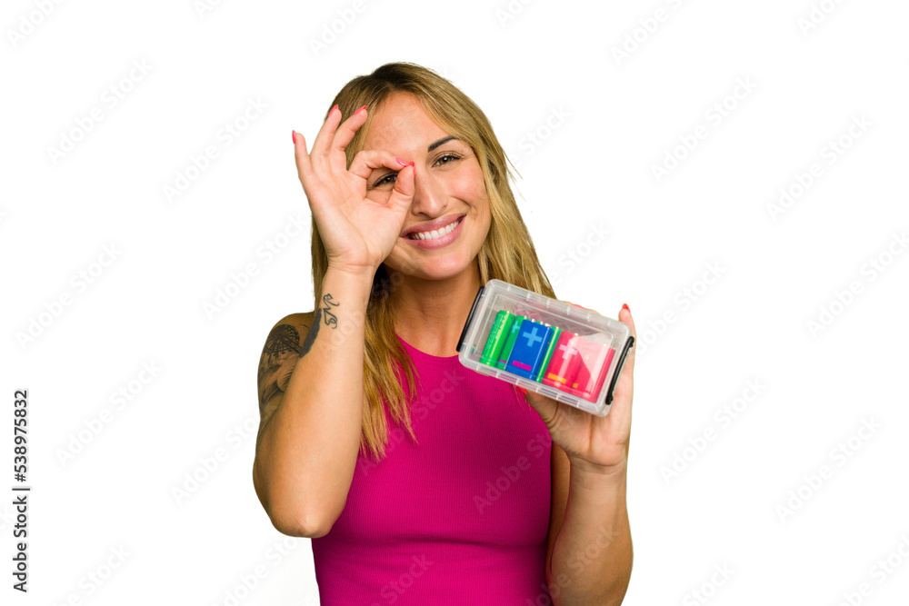 Young caucasian woman holding battery box isolated on green chroma background excited keeping ok gesture on eye. Young caucasian woman holding battery box isolated on green chroma background excited keeping ok gesture on eye.