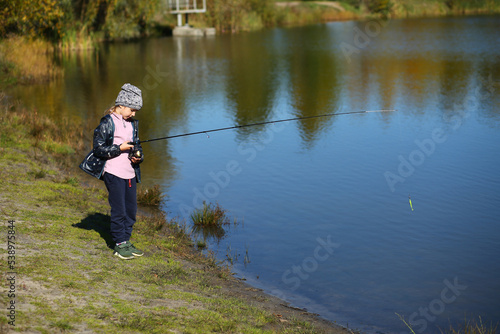 Six year old girl fishing on the autumn lake with a fishing rod