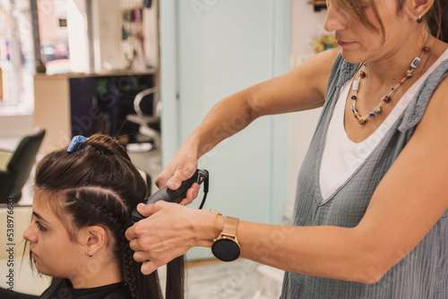 Young Woman Straightening Her Hair At The Hairdresser's.
Hairdresser Using A Modern Flat Iron To Style A Client's Hair At The Hairdresser's Salon