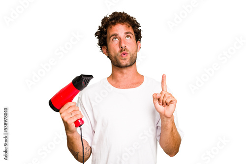 Young caucasian man holding an hairdryer isolated pointing upside with opened mouth.