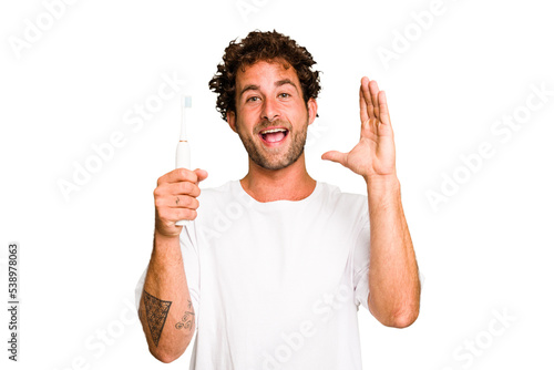 Young caucasian man holding an electric toothbrush isolated receiving a pleasant surprise, excited and raising hands.