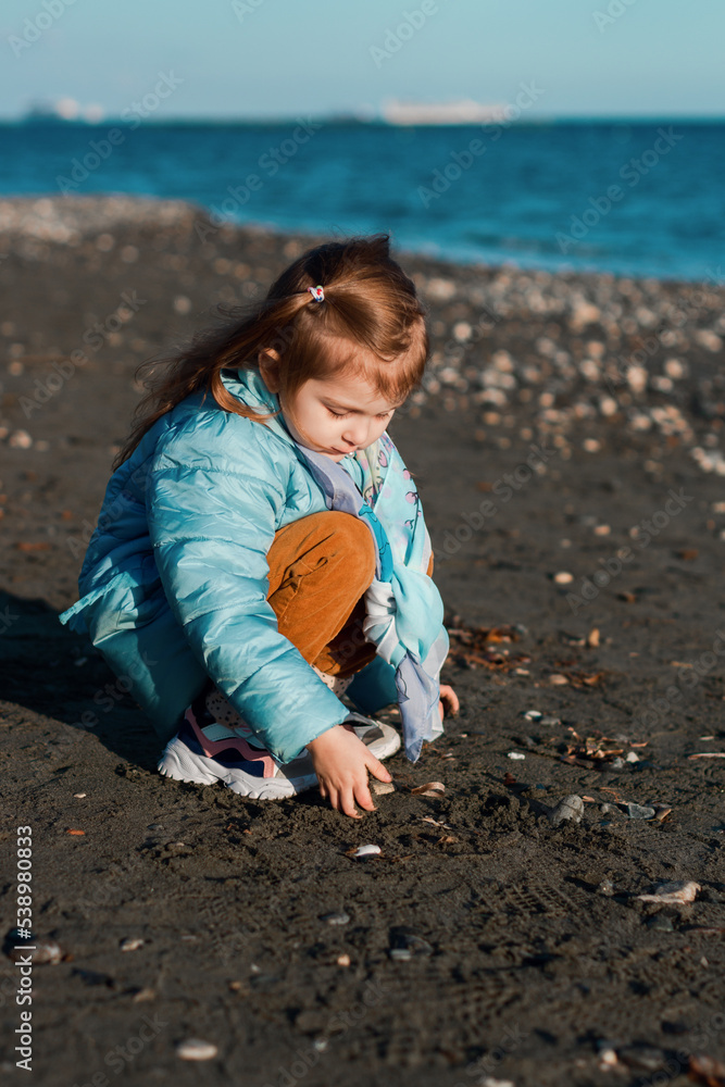 Little girl wear blue jacket walking on beach, enjoying sunny autumn spring day Little girl wear blue jacket walking on beach, enjoying sunny autumn spring day
