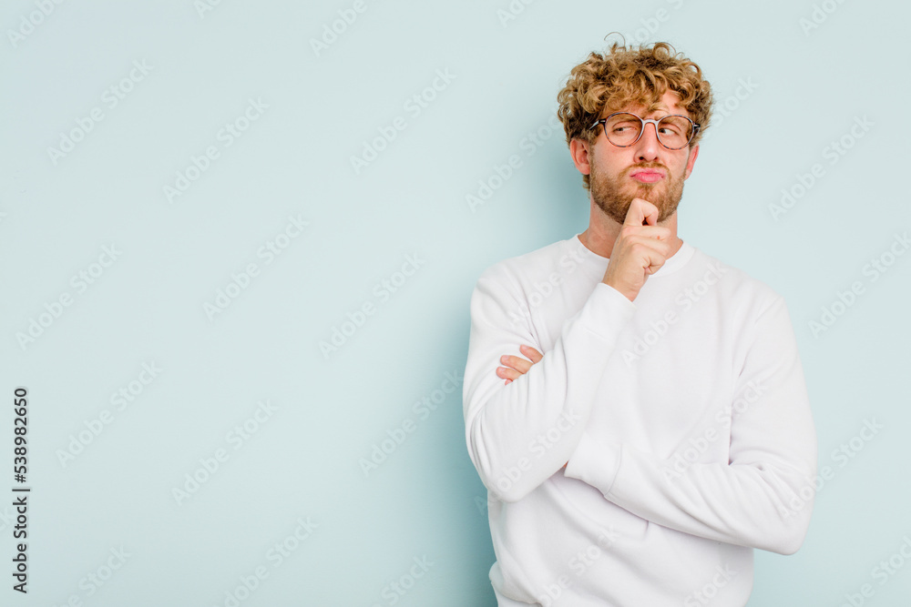 Obraz premium Young caucasian man isolated on blue background looking sideways with doubtful and skeptical expression.