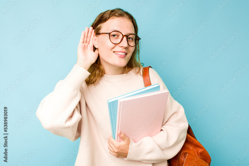 Young student caucasian woman isolated on blue background trying to listening a gossip.