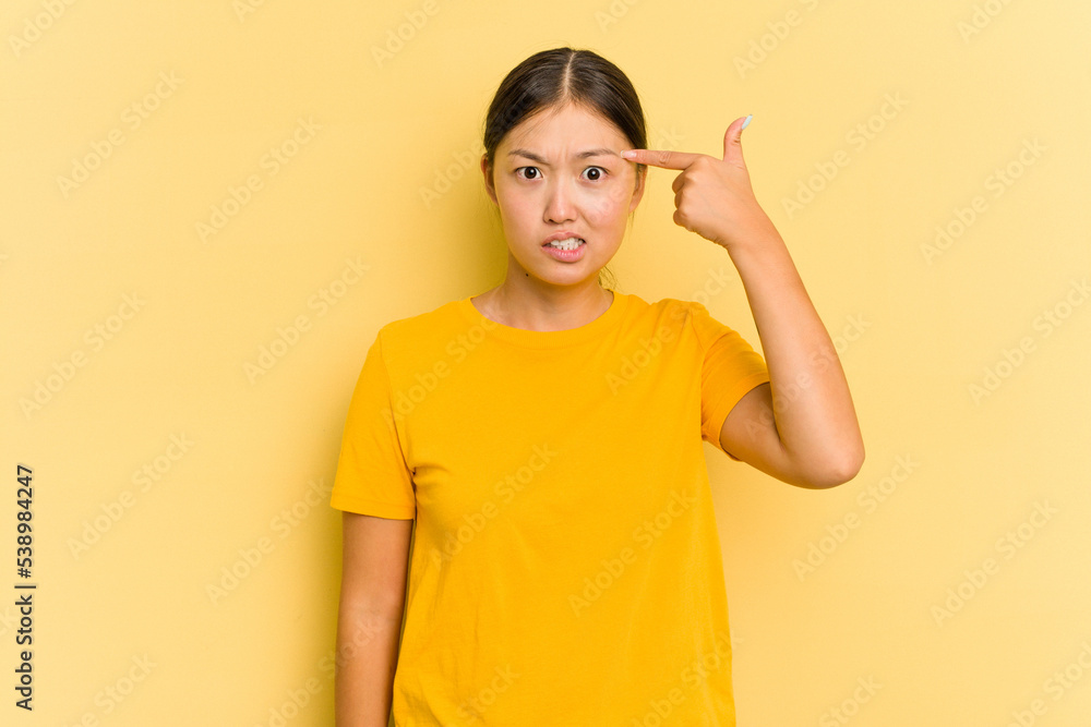 Young Asian woman isolated on yellow background showing a disappointment gesture with forefinger. Young Asian woman isolated on yellow background showing a disappointment gesture with forefinger.