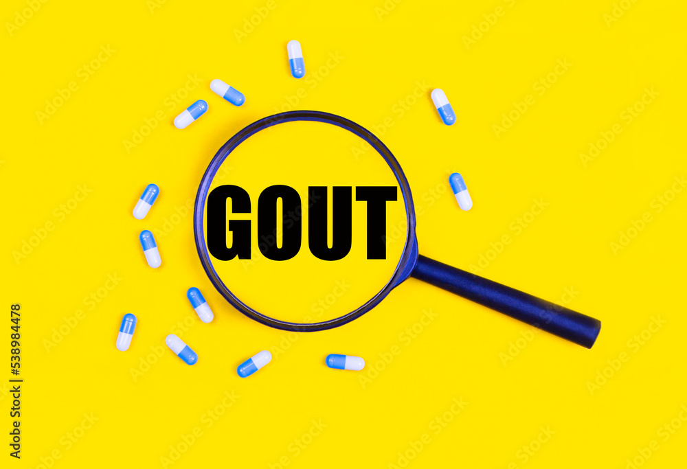 Pharmaceutical tablets and capsules near a magnifying glass with the text GOUT on a yellow background. View from above.