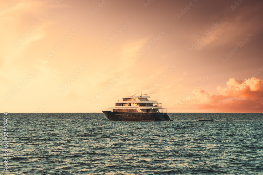 View of a luxury yacht floating on the waves with a stunning evening skyscape in the background; a multideck safari boat in the ocean on a sunset with a dramatic sky of a golden hour