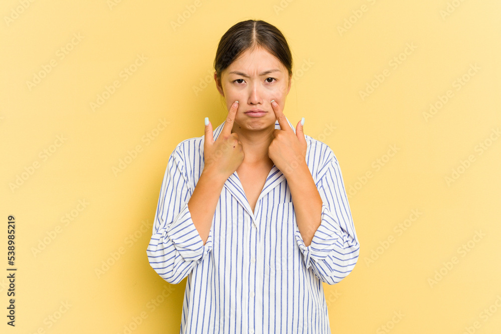 Young Asian woman isolated on yellow background crying, unhappy with something, agony and confusion concept. Young Asian woman isolated on yellow background crying, unhappy with something, agony and confusion concept.