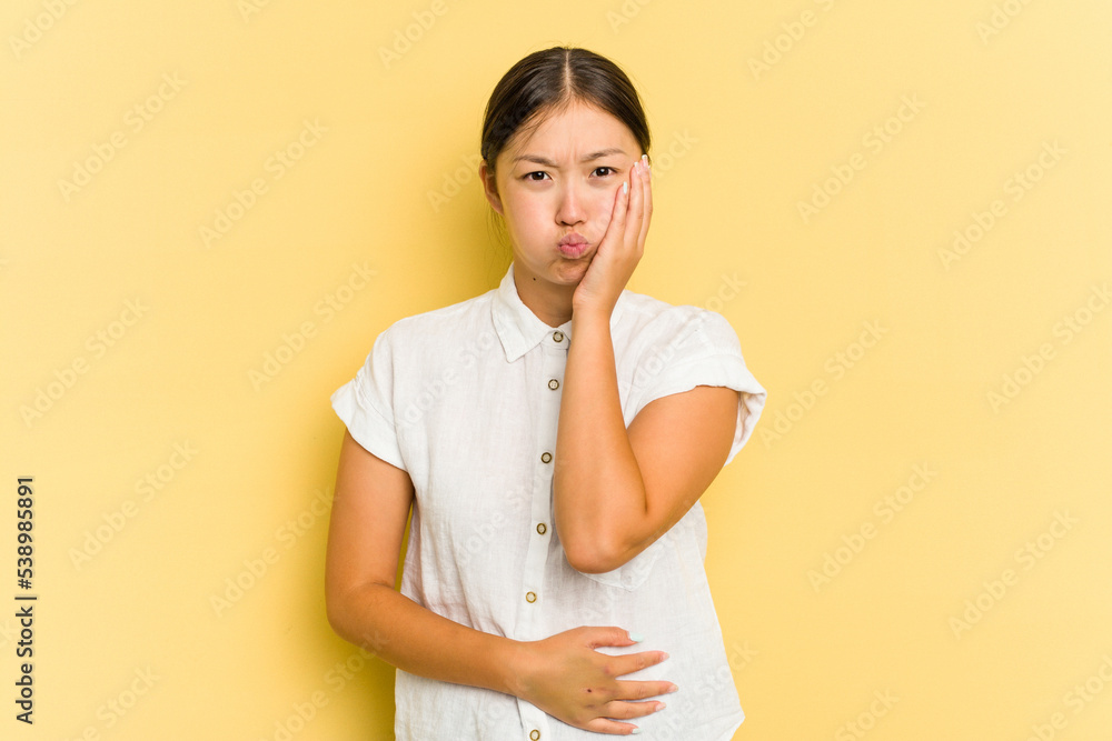 Young Asian woman isolated on yellow background blows cheeks, has tired expression. Facial expression concept. Young Asian woman isolated on yellow background blows cheeks, has tired expression. Facial expression concept.