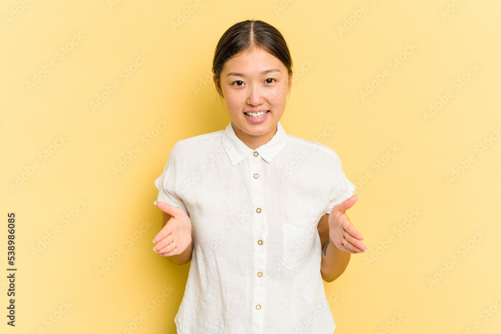 Young Asian woman isolated on yellow background holding something with both hands, product presentation. Young Asian woman isolated on yellow background holding something with both hands, product presentation.