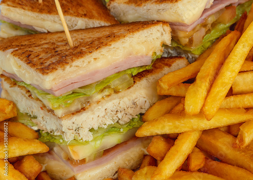Three-tier sandwich with chicken, ham, lettuce, tomato and cheese, accompanied by French fries, also called a club sandwich photo