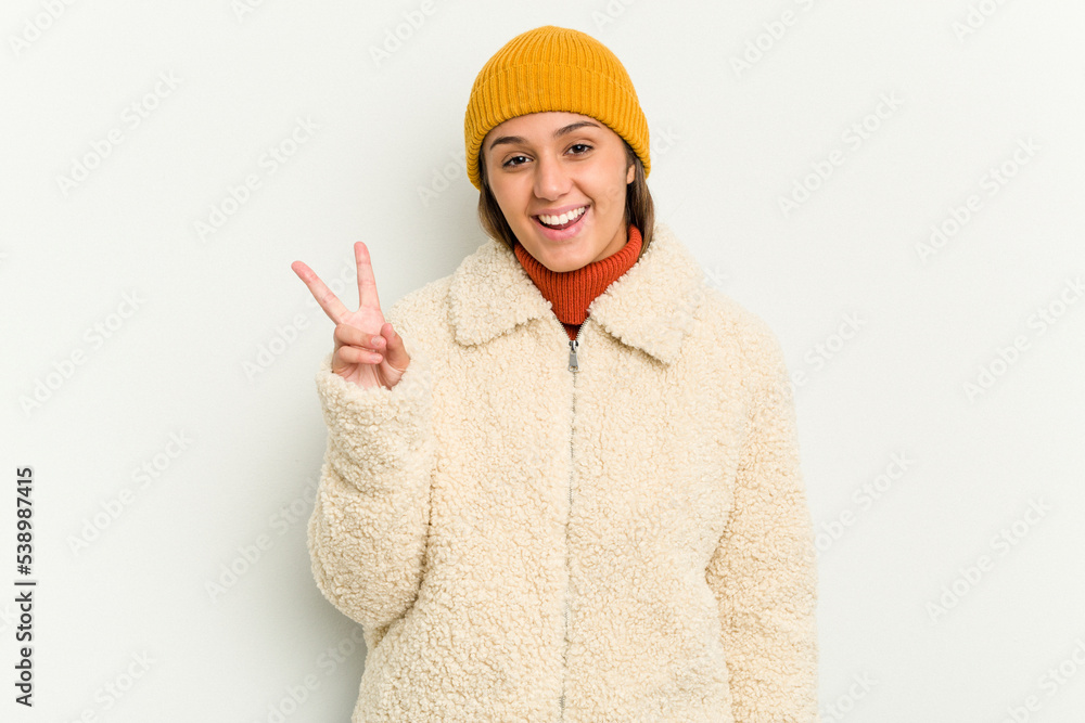 Young Indian woman wearing winter jacket isolated on white background joyful and carefree showing a peace symbol with fingers.