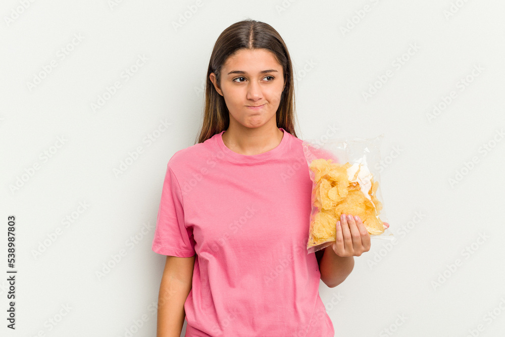 Young Indian woman holding crips isolated on white background confused, feels doubtful and unsure. Young Indian woman holding crips isolated on white background confused, feels doubtful and unsure.