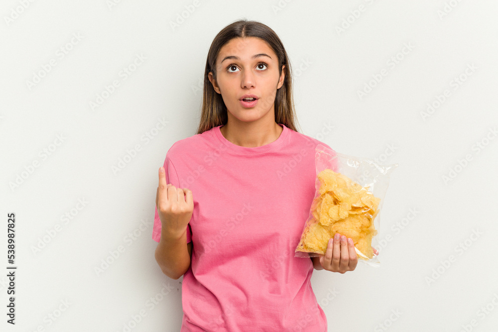 Young Indian woman holding crips isolated on white background pointing upside with opened mouth. Young Indian woman holding crips isolated on white background pointing upside with opened mouth.