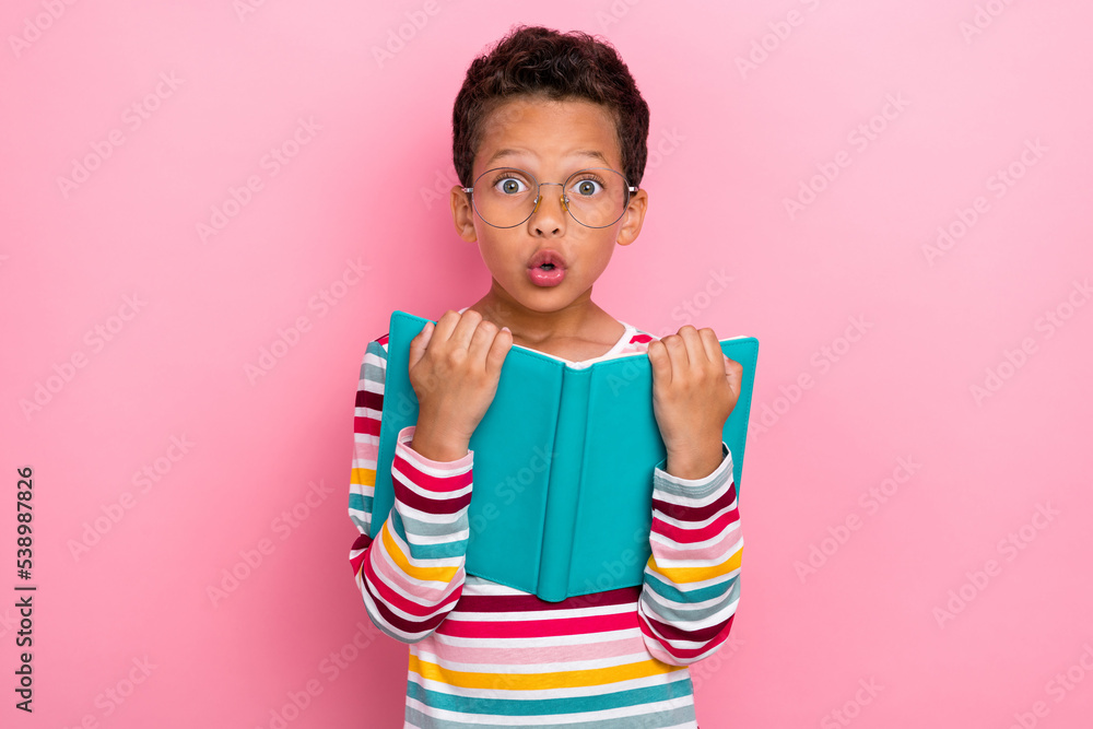 Photo of nice charming schoolboy wavy hairstyle wear striped long sleeve hold book staring pouted lips isolated on pink color background Photo of nice charming schoolboy wavy hairstyle wear striped long sleeve hold book staring pouted lips isolated on pink color background
