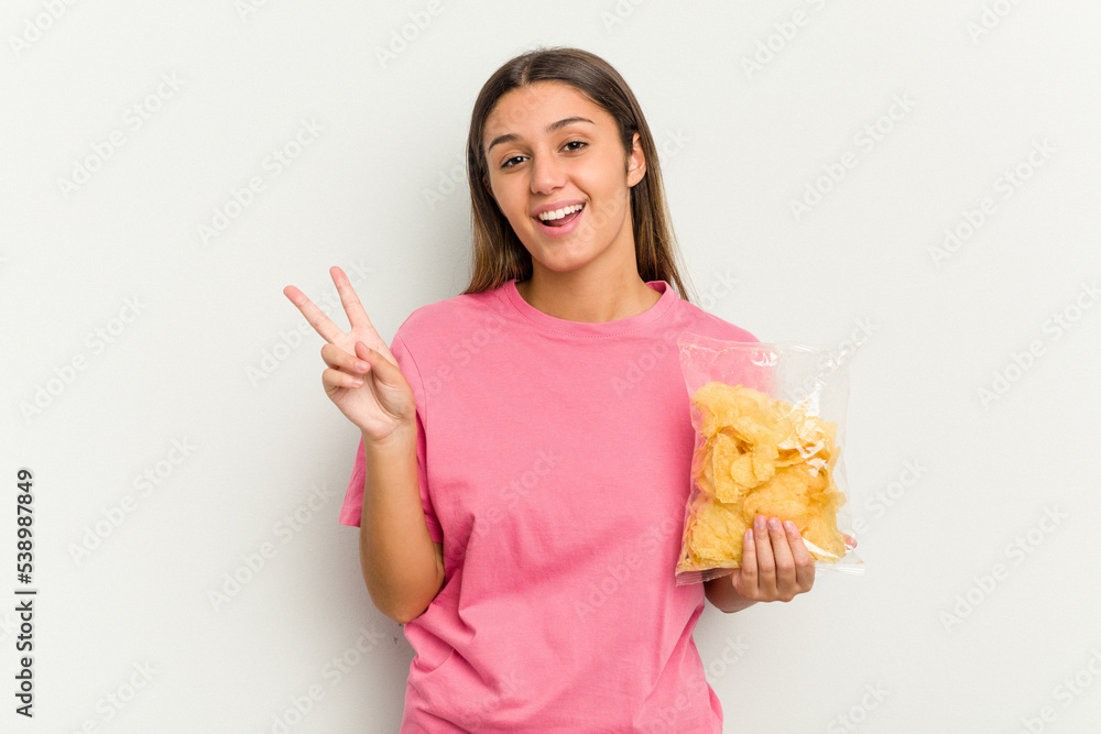 Young Indian woman holding crips isolated on white background joyful and carefree showing a peace symbol with fingers. Young Indian woman holding crips isolated on white background joyful and carefree showing a peace symbol with fingers.