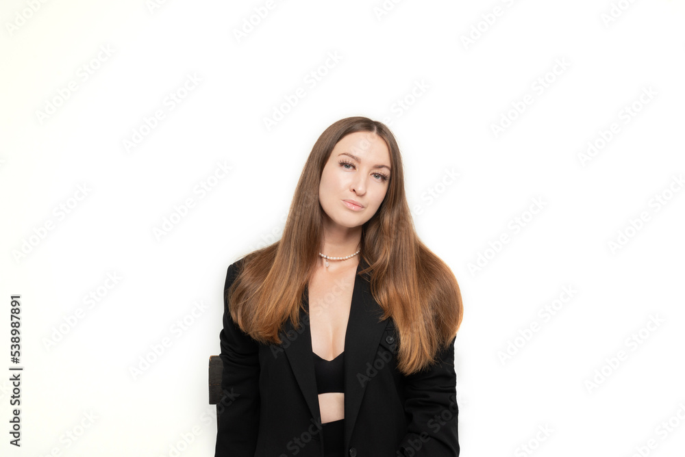 A beautiful long-haired girl dressed in a black jacket, bra and trousers sits on a chair in a photo studio on a white background A beautiful long-haired girl dressed in a black jacket, bra and trousers sits on a chair in a photo studio on a white background