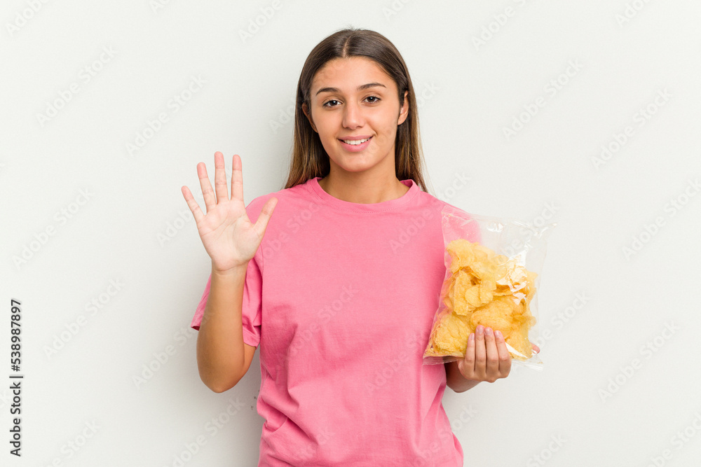 Young Indian woman holding crips isolated on white background smiling cheerful showing number five with fingers. Young Indian woman holding crips isolated on white background smiling cheerful showing number five with fingers.