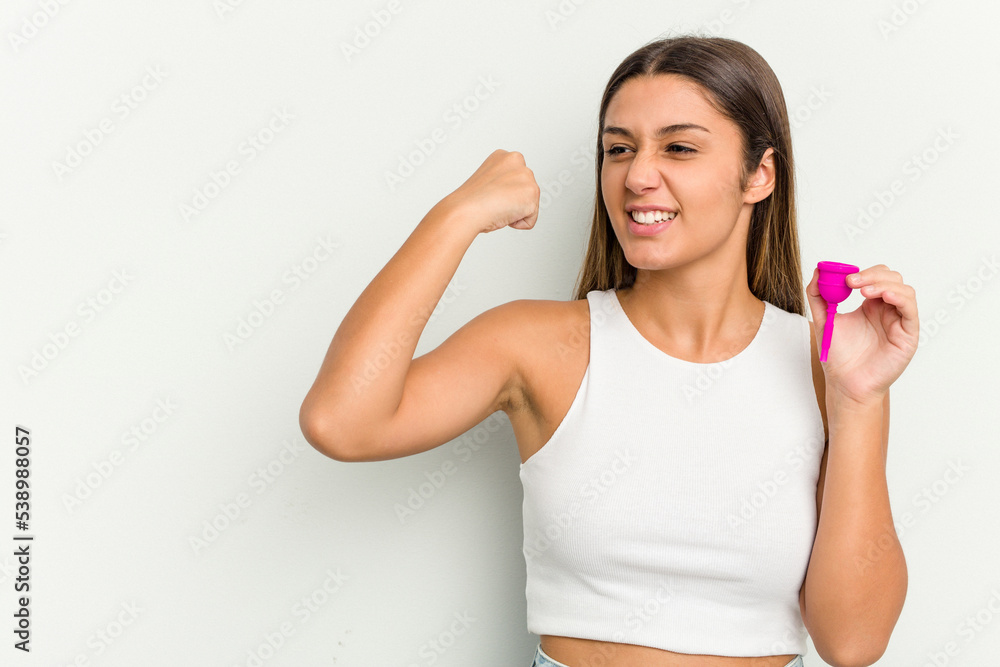 Young woman holding a menstrual cup isolated on white background raising fist after a victory, winner concept. Young woman holding a menstrual cup isolated on white background raising fist after a victory, winner concept.