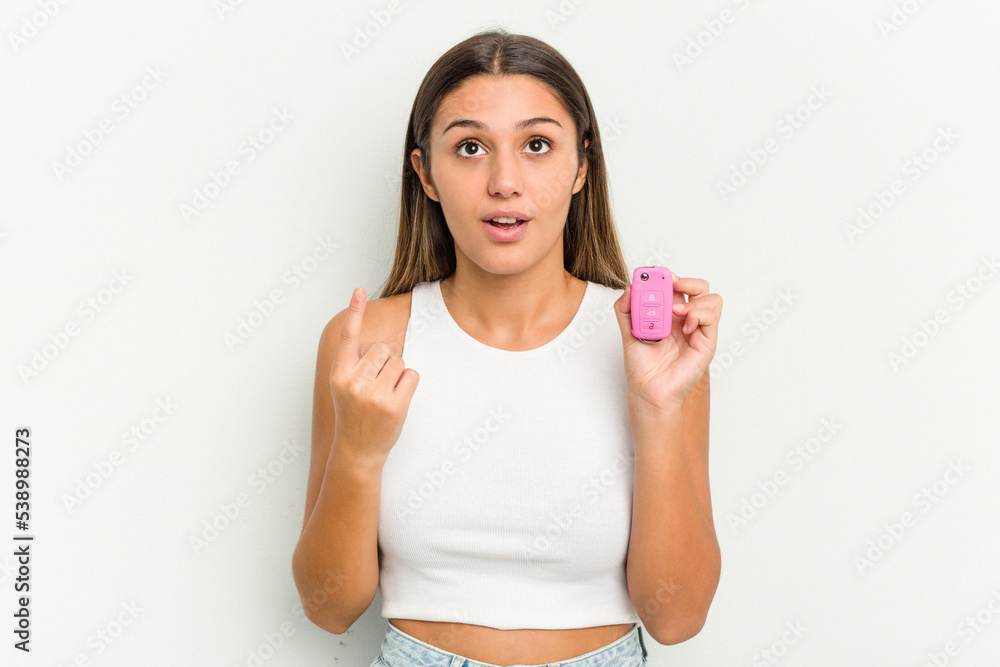 Young indian woman holding an electronic pink car keys pointing upside with opened mouth. Young indian woman holding an electronic pink car keys pointing upside with opened mouth.