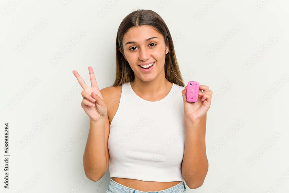 Young indian woman holding an electronic pink car keys joyful and carefree showing a peace symbol with fingers. Young indian woman holding an electronic pink car keys joyful and carefree showing a peace symbol with fingers.